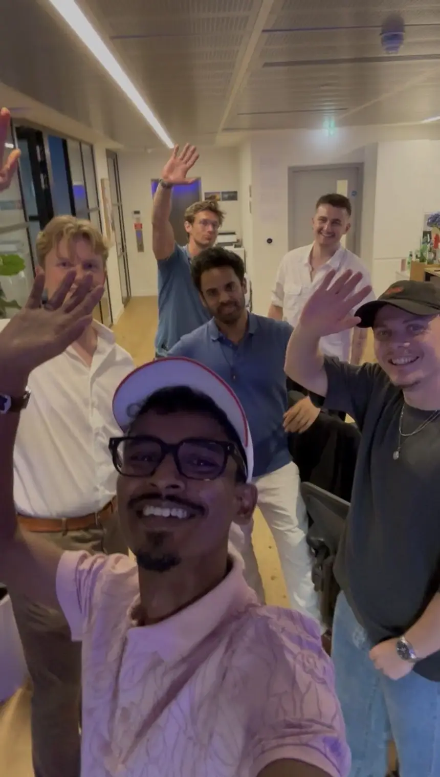Vasu with a group of people in an office, everyone waving at the camera.