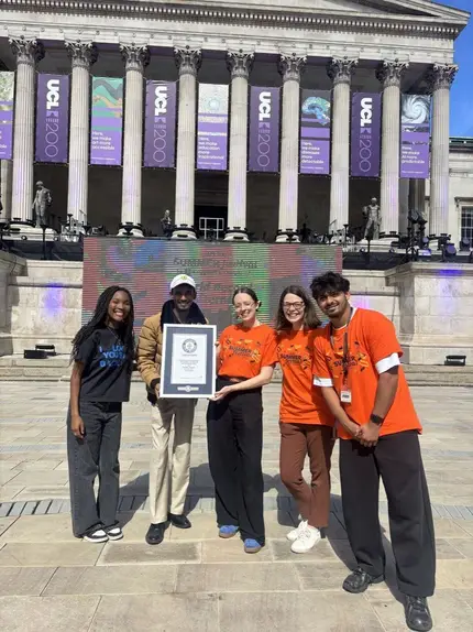 A group outside a university building holding a framed certificate.