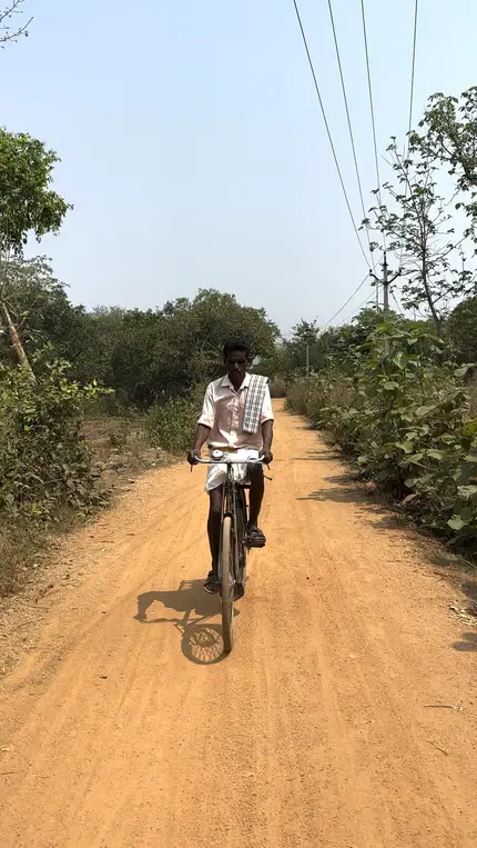 A red dirt road running through fields near the village, with someone cycling along it.